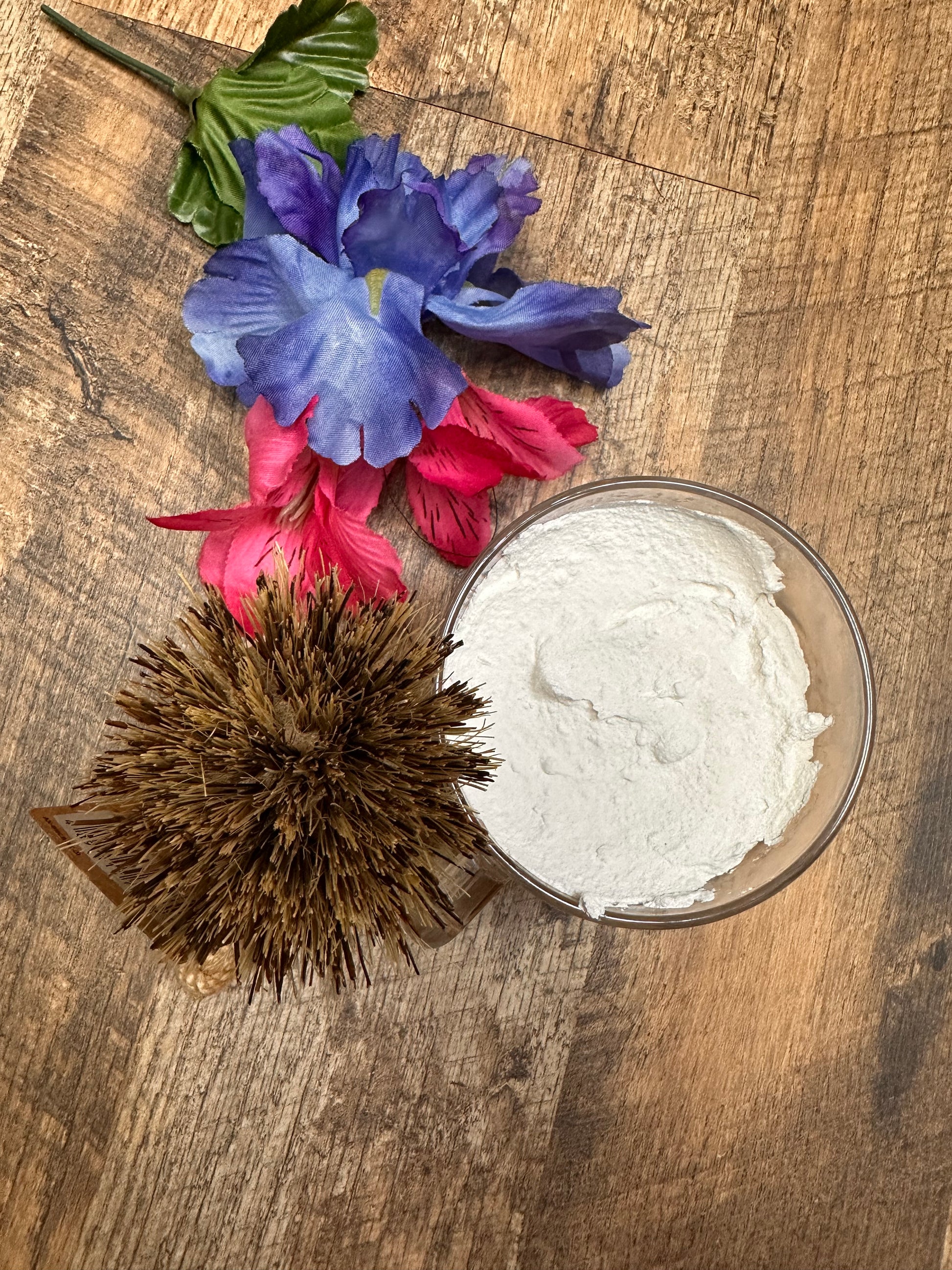 Bowl of white dish soap  with flowers and a brush on a wooden surface